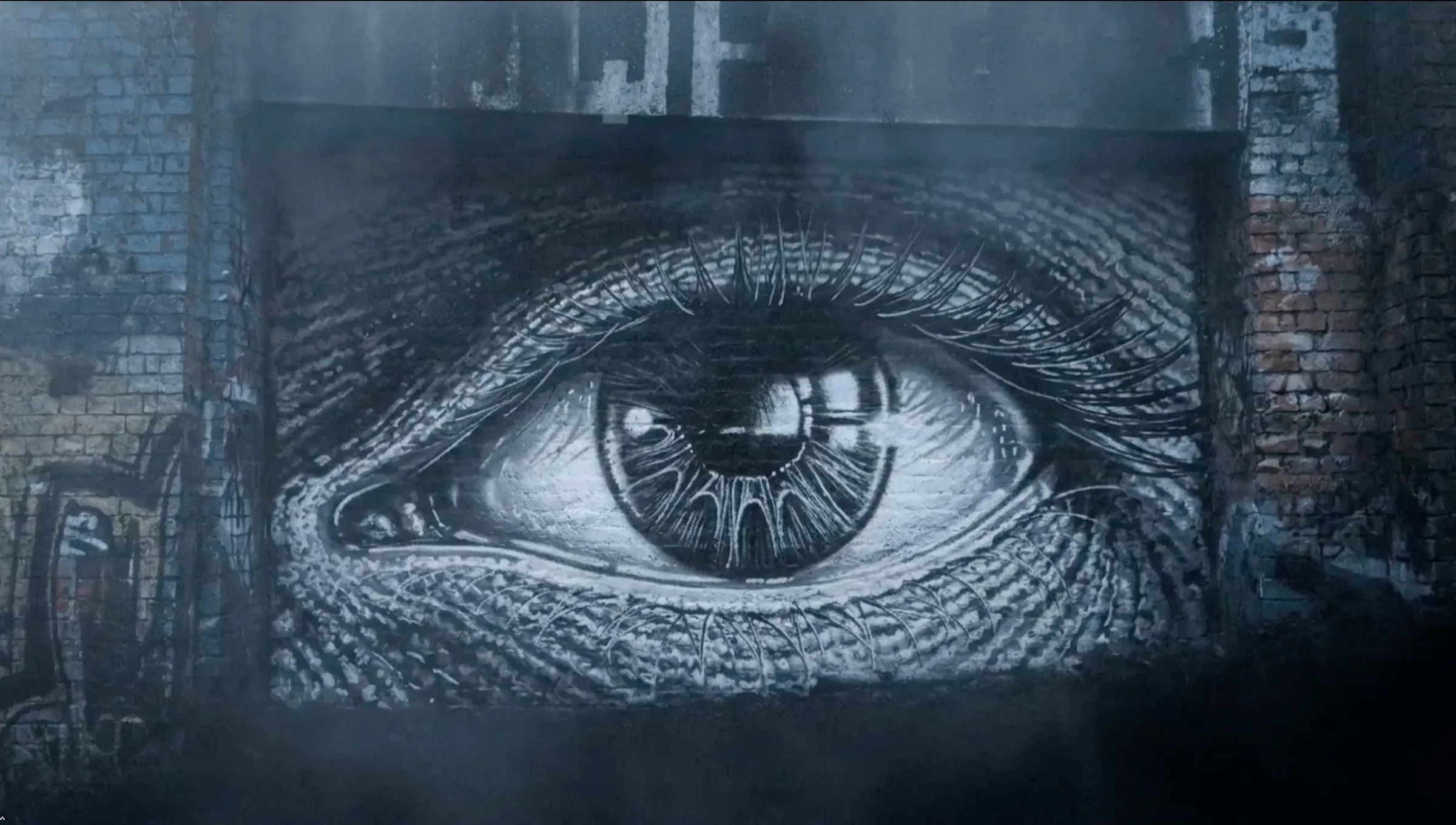 A large eye painted in black and white on a brick railway wall.