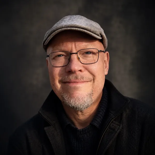 Portrait of the author Thomas Ludlow, wearing a flat cap and glasses.